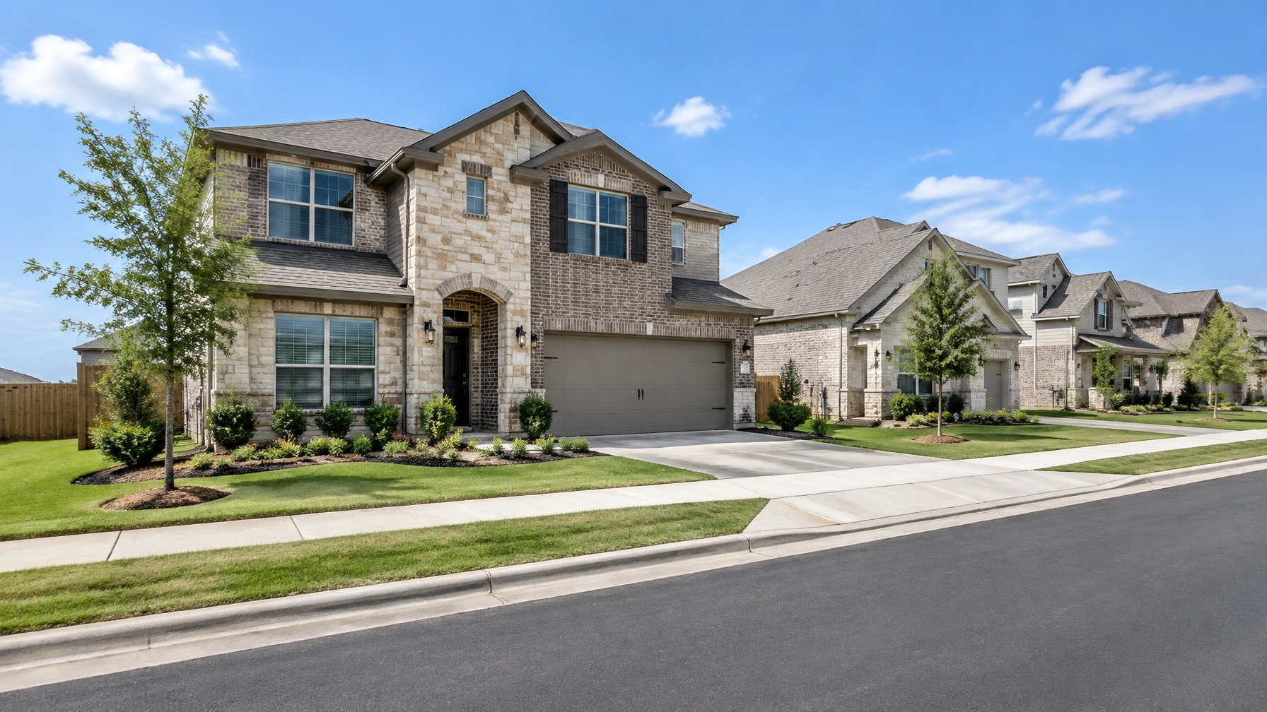 Newer brick-and-stone suburban homes with manicured lawns along a broad residential street