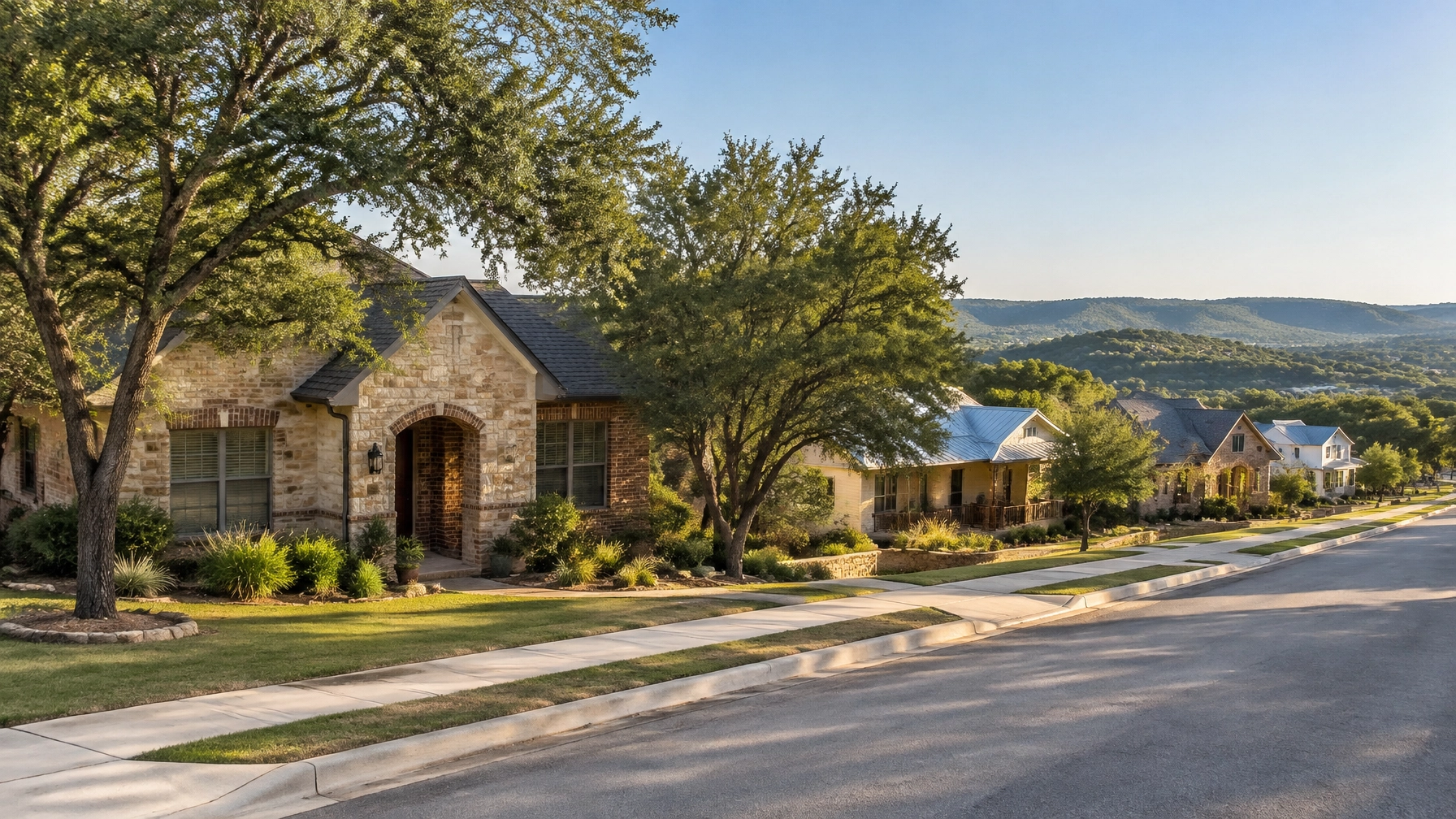 Hill Country neighborhood street with limestone homes, mature trees, and rolling hills beyond